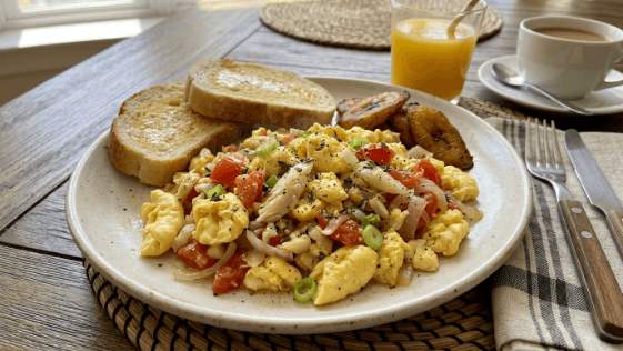 Cooked ackee served with saltfish, tomatoes and onions on a plate, its soft pale yellow pieces resembling scrambled egg